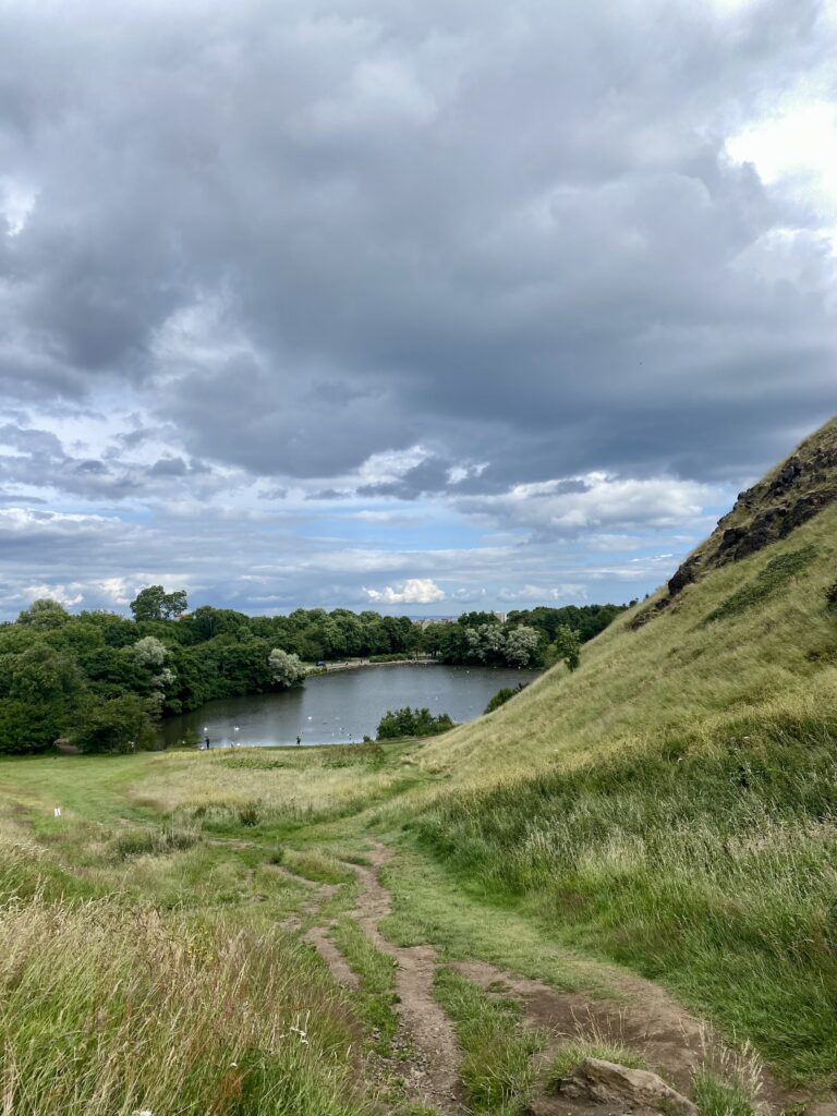 The grassy hill of Arthur's Seat overlooking a lake.